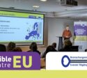 Accessible EU och Branschorganisationen Svensk Tillgänglighets logotyper. I bakgrunden står en teckenspråkstolk på en scen bredvid en projektorduk och en talare.